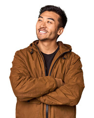 Young Chinese man in studio background smiling confident with crossed arms.