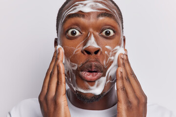 Close up shot of dark skinned bearded man applying cleansing beauty product on face using facial...