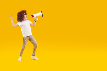 Happy preteen boy shouting into megaphone making announcement. Full length portrait of happy boy in white shirt and jeans holding megaphone screaming into empty space over isolated background - obrazy, fototapety, plakaty