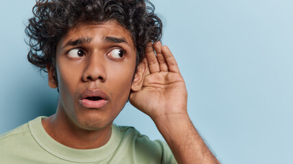 Worried curious Hindu man keeps hand near ear tries to overhear information listens someone...