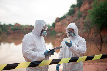 Two men wearing PPE stood looking at glass bottles in their hands. To check for contaminants in the...
