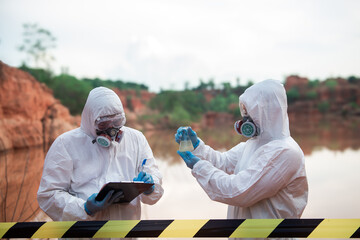 Two men wearing PPE stood looking at glass bottles in their hands. To check for contaminants in the...