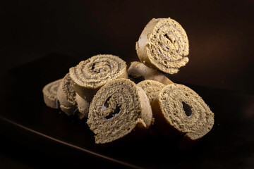 Delicious sweet dessert coconut sponge cake roll slices are arranged on a black ceramic platter...
