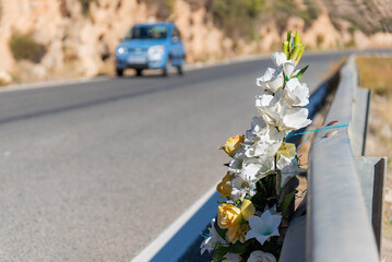 Bouquet of flowers tied to a road guardrail in memory of a person who died in an accident with a car driving nearby. - obrazy, fototapety, plakaty
