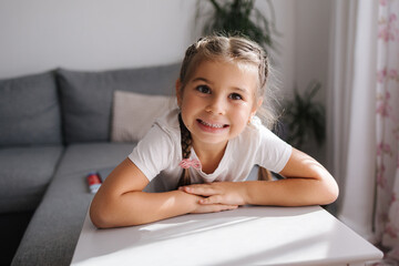 Happy adorable little girl sitting at the table and smile. Beautiful five year old girl at home.