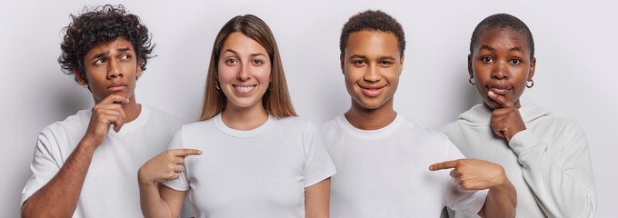 Set of four young people dressed in casual t shirts point at mock up space of t shirts stand in...