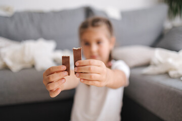 Little crafty girl eats sweets at home. Kid eating chocolate and have fun. Chaos at home. Focus on...