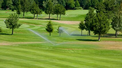 Automatic high-pressure water sprinkler at green golf course watering the grass.