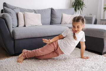 Active and energetic little girl have fun and home. Living room. Kid sitting on the carpet.