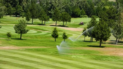 Automatic high-pressure water sprinkler at green golf course watering the grass.