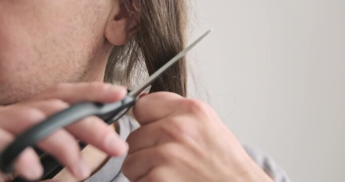 Cutting your own hair. Close-up of man cutting off lock of hair with scissors. Home hair salon concept, do it yourself, space for text.