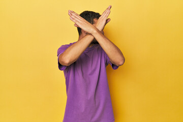 Young Hispanic man on yellow background keeping two arms crossed, denial concept.