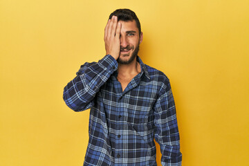 Young Hispanic man on yellow background having fun covering half of face with palm.