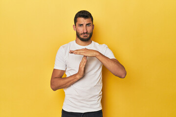 Young Hispanic man on yellow background showing a timeout gesture.