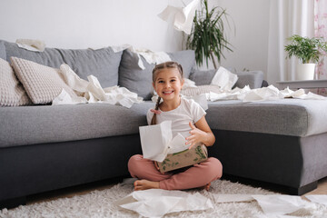 The process of creating a mess by a child. Little girl scatters napkins in living room