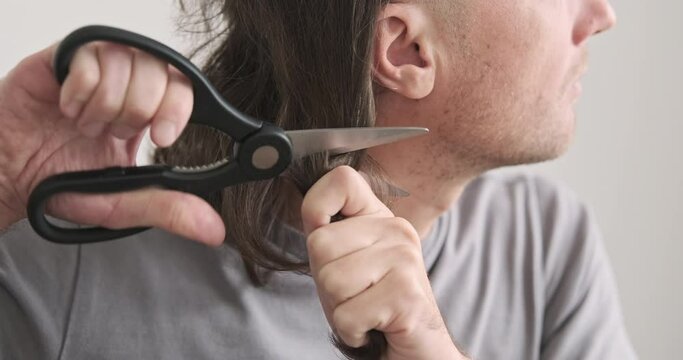 Cutting your own hair, profile head, side view. Close-up of man cutting off lock of hair with scissors. Home hair salon concept, do it yourself