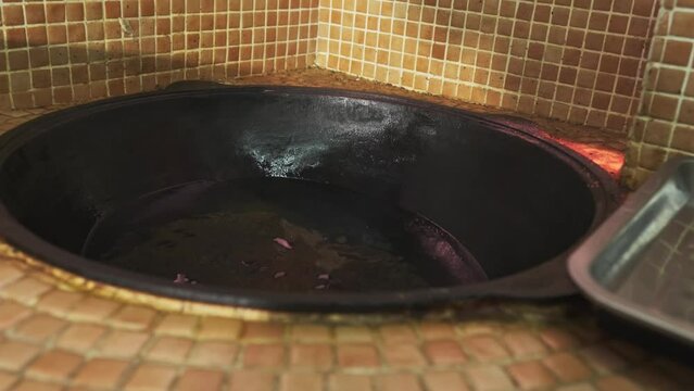 The chef puts pieces of meat with a slotted spoon into the oil boiling in a large pilaf cauldron