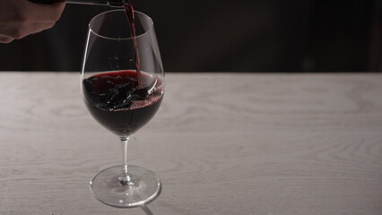 Pour red wine into wineglass on white oak table with copy space