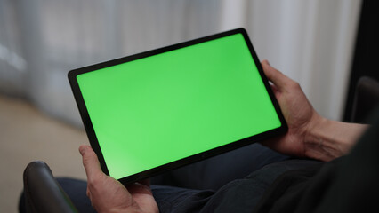 Man sitting indoors on a chair with tablet pc with green screen - Powered by Adobe