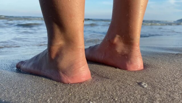 Close up view back of female heel feet standing on sand seashore sunny day. Walking towards the ocean in slow motion. Back view.