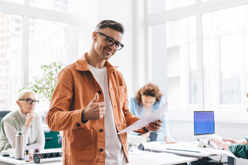 Positive man with documents showing thumb up in office