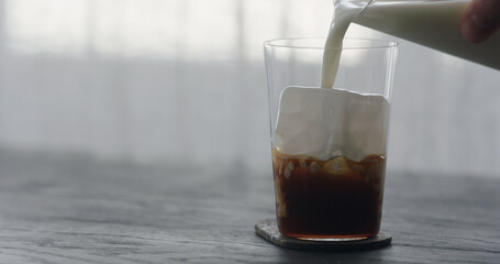 pour milk into ice coffee on black wood table
