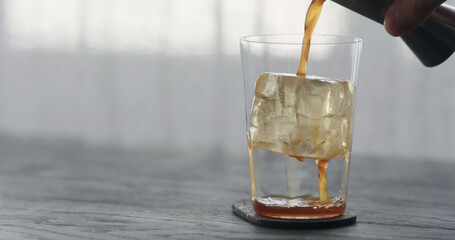 coffee pour over ice cube in tumbler glass on black wood table