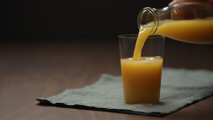 pour cold pressed organic orange juice into tumbler glass on wood table