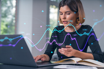 Pensive attractive beautiful businesswoman in working on laptop, talking phone, office workplace in background. Forex graph and charts hologram icons. Concept of market trading and research.