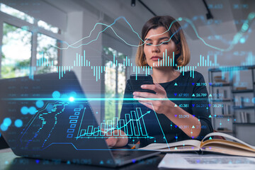 Pensive attractive beautiful businesswoman in working on laptop, talking phone, office workplace in background. Forex graph and charts hologram icons. Concept of market trading and research.