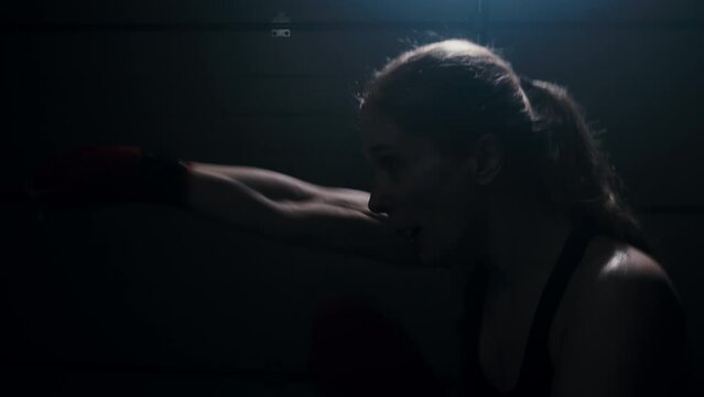 Woman boxer in dark room practicing shadow boxing, female fighter practicing fast punches with back light in, 4k
