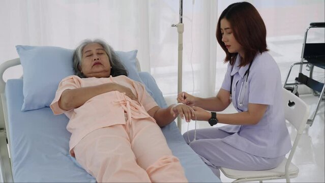 Female nurse takes care of inserting an IV line for an elderly Asian female patient.