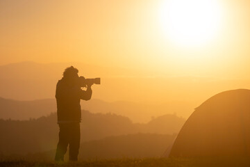 Fototapeta na wymiar Photographer is taking landscape photo by the tent during overnight camping at the beautiful scenic sunrise over the mountain for outdoor adventure vacation travel