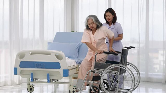 A nurse carries an elderly Asian patient into a wheelchair to take him to get an x-ray of his leg injured in an accident.