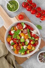Caprese salad with cherry tomatoes, mini mozzarella balls, avocado, pesto sauce and fresh basil. Healthy vegetarian meal.