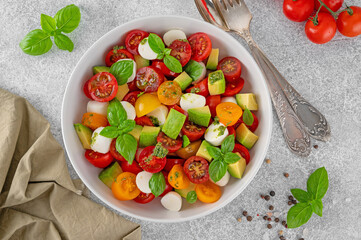 Caprese salad with cherry tomatoes, mini mozzarella balls, avocado, pesto sauce and fresh basil. Healthy vegetarian meal.
