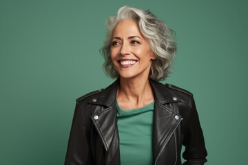 Portrait of a joyful woman in her 50s sporting a classic leather jacket against a pastel green...