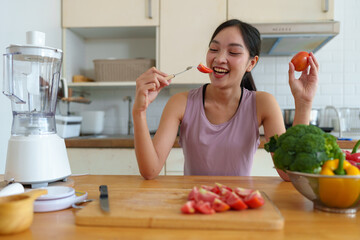 Beautiful young woman in exercise clothes is cutting tomatoes to eat for good skin and health. Refreshing after a happy workout inside the house. Food concept. Vegetables, useful fruits. Lifestyle.