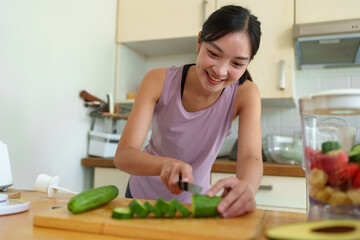 Obraz na płótnie Canvas Confident young woman preparing vegetable salad in kitchen, healthy food vegetarian salad Healthy lifestyle cooking at home, preparing vegetables, fruits cut cucumber ingredients on the cooking table