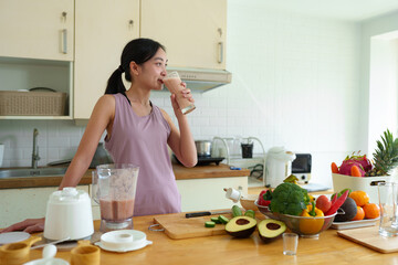 Young woman in Asian exercise clothes making a fruit and vegetable smoothie after a healthy workout at home. Concept of diet and healthy food, lifestyle