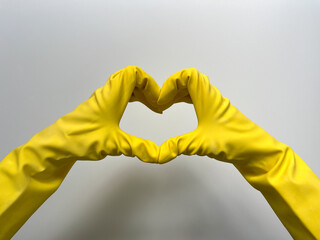 Hands in yellow rubber cleaning gloves make a heart. 