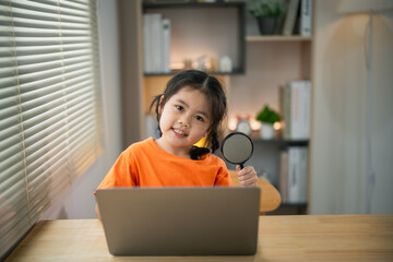 Asian baby kid girl holding magnifying glass and using laptop education to get good ideas, children and school concept - happy smiling student girl learning studying. Education development concept.