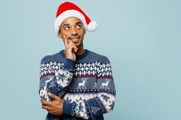 Young man wear knitted sweater Santa hat posing put hand prop up on chin, lost in thought and...