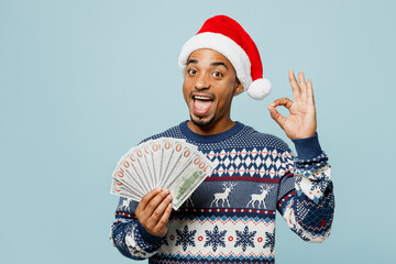 Young man wear knitted sweater Santa hat posing hold fan of cash money in dollar banknote show ok...