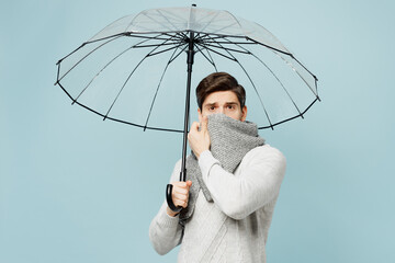Young sad ill sick man wear gray sweater hold umbrella cover mouth with scarf isolated on plain...