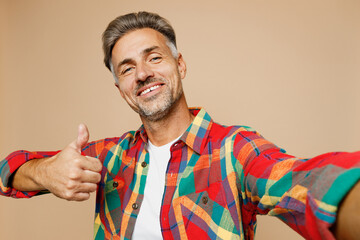 Close up adult fun man he wear red shirt white t-shirt casual clothes doing selfie shot pov on mobile cell phone show thumb up isolated on plain pastel light beige color background. Lifestyle concept.