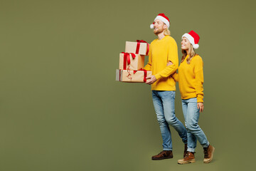 Full body merry young couple two friends man woman wears sweater Santa hat posing hold stack of present box with gift ribbon bow go isolated on plain green background Happy New Year Christmas concept