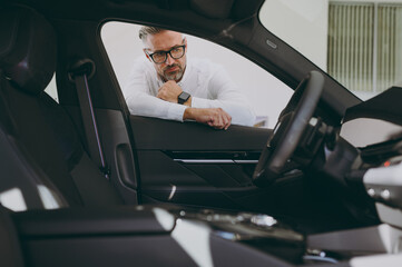 Minded pensive adult man customer buyer client wear shirt looking inside car check interior choose...