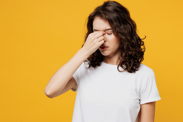 Young sad tired exhausted Caucasian woman wear white blank t-shirt casual clothes keep eyes closed rub put hand on nose isolated on plain yellow orange background studio portrait. Lifestyle concept.