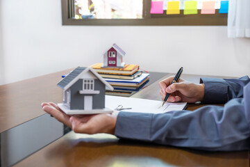 Real estate agents hand use pen, holding home model, explains the business contract for signing a business contract, renting, buying, mortgage, loan or home insurance